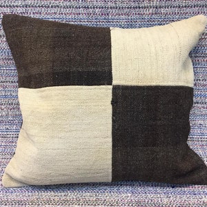 May include: A square-shaped cushion with a chequered pattern in brown and white. The cushion is made of a woven fabric and has a soft, textured surface.