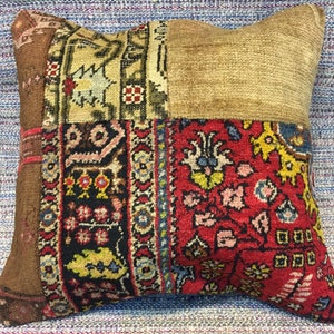 Könnte beinhalten: Dekoratives quadratisches Kissen mit Patchwork-Design. Das Kissen hat Abschnitte aus braunem, beigem und rotem Stoff mit komplizierten Mustern. Das Kissen liegt auf einer blau-weiß gestreiften Oberfläche.
