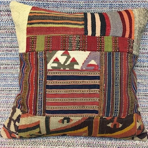 May include: A square patchwork pillow with a variety of colorful stripes and patterns in shades of red, blue, green, brown, and white.