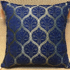 May include: A blue and gold decorative throw pillow with a tassel on each corner. The pillow has a geometric pattern with a floral design.