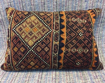 May include: A rectangular pillow with a geometric pattern in shades of brown, orange, and black. The pillow is made of woven fabric and has a fringe border.