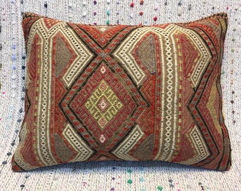May include: A rectangular pillow with a geometric pattern in shades of red, brown, beige, and white. The pillow is made of woven fabric and has a traditional design.