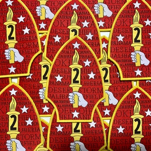 May include: A close-up of several red and yellow embroidered patches with the number "2" and the words "DESERT STORM" and "JALIBA" in white. The patches are arranged in a pile, with the top patch facing the camera.