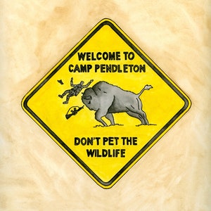 May include: A yellow diamond-shaped warning sign with black text and a cartoon illustration. The sign reads "Welcome to Camp Pendleton Don't Pet the Wildlife". The illustration shows a soldier being tossed by a bison.