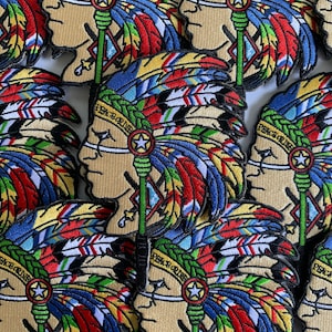 Pode incluir: Patches bordados com um perfil nativo americano com um cocar de penas em vermelho, azul, amarelo e verde. Os patches têm o texto "PEACE OR DIE" e um emblema de estrela. Os patches são bege e têm um fundo branco.