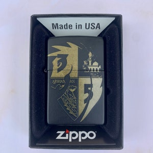 Puede incluir: Encendedor Zippo negro con un diseño dorado que presenta un escudo con las palabras "Afganistán" e "Irak" y el número "5". El encendedor está en una caja negra con las palabras "Made in USA" y "Zippo" impresas en ella.