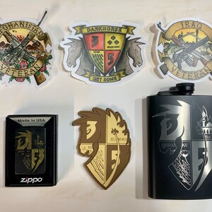 Puede incluir: Una petaca de metal negro con un diseño grabado en plata que presenta una cabeza de caballo y dos escudos. Los escudos tienen las palabras "AFGHAN" e "IRAQ" en ellos. La petaca está rodeada de cinco pegatinas, incluyendo dos con las palabras "VETERAN" y "GET SOME".