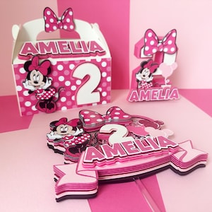Op de afbeelding: Roze en witte taarttopper met een Minnie Mouse-figuur, het cijfer 2 en de naam Amelia. De topper is gelaagd en heeft een stippenpatroon.