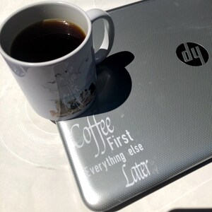 May include: A white coffee mug with a black coffee inside and a gray laptop with the text "Coffee First Everything Else Later" on the lid. The laptop has a HP logo on the lid.