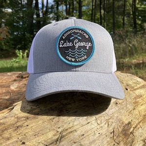 May include: Gray and white trucker hat with a black and blue patch that says "Adirondacks Lake George New York" with a pair of crossed oars.