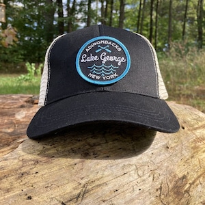 May include: Black and white trucker hat with a blue and white embroidered patch that says "Adirondacks Lake George New York" with a pair of crossed oars.