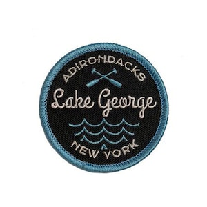 May include: A blue and black embroidered patch with the text "Adirondacks Lake George New York" and a pair of crossed oars.
