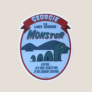 May include: A blue and red circular sticker with the text "Georgie the Lake George Monster" and a cartoon illustration of a green lake monster with a toothy grin. The text below the monster reads "An epic hoax... or is there a splash of truth to this legendary leviathan?"
