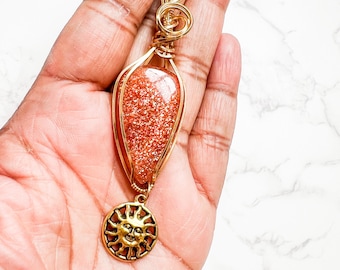 May include: Gold wire wrapped pendant featuring a teardrop-shaped sunstone with a gold sun charm.