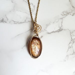 May include: A gold chain necklace with a pendant featuring a sunstone cabochon set in a wire wrapped oval frame.