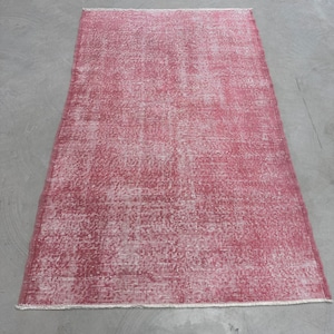 May include: A vintage-style rug with a faded red color and a white, textured pattern. The rug has a frayed edge.