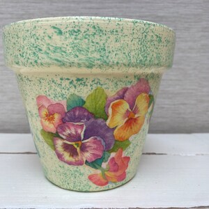 Könnte beinhalten: Ein weißer Keramik-Blumentopf mit grüner, gesprenkelter Glasur und einem Blumendesign mit rosa, lila und gelben Stiefmütterchen.