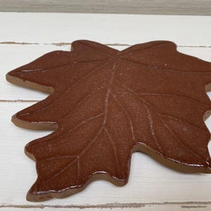 Könnte beinhalten: Ein braunes Keramik-Ahornblatt mit detaillierten Adern. Das Blatt ist ein dekorativer Akzent für Haus oder Garten.