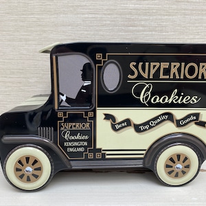 Puede incluir: Lata de galletas de camión de reparto vintage en blanco y negro con las palabras "Superior Cookies" en letras doradas. La lata tiene una franja blanca con las palabras "Best Top Quality Goods" en letras doradas.