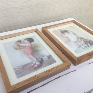 Könnte beinhalten: Zwei gerahmte Bilder von Kindern mit Hunden. Das Bild links zeigt ein Mädchen, das einen kleinen braunen Hund hält. Das Bild rechts zeigt ein Mädchen mit einem braunen und weißen Hund.