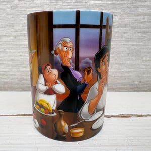 May include: A cylindrical ceramic mug featuring a colorful illustration of animated characters. The design includes a dining scene with figures in a room with a window. The mug has a brown background with a blue sky.
