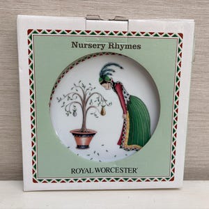 Peut inclure: Une assiette décorative de la collection Royal Worcester Nursery Rhymes. L'assiette représente une femme en robe verte et un poirier. La boîte a un fond vert avec les mots "Nursery Rhymes" et "Royal Worcester".