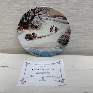 Könnte beinhalten: Ein dekorativer Teller mit einer Winterszene mit Figuren in einer verschneiten Landschaft. Der Teller hat eine runde Form und eine detaillierte Malerei. Unter dem Teller befindet sich ein Echtheitszertifikat mit dem Text "Please Dig Me Out".