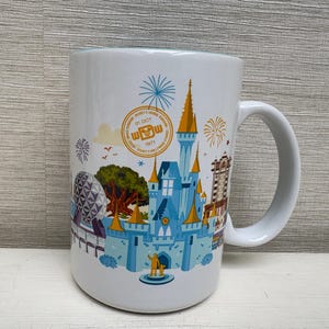 Könnte beinhalten: Weißer Keramikbecher mit einer farbenfrohen Illustration eines Schlosses, einer Kugel und anderer Wahrzeichen. Der Becher hat einen Henkel und enthält den Text "WDW" und "01 OCT 1971". Das Design umfasst Feuerwerk und andere dekorative Elemente.