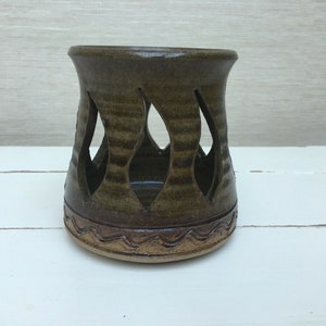 Könnte beinhalten: Ein brauner Kerzenhalter aus Keramik mit einem ausgeschnittenen Design. Der Halter hat einen gewellten Rand und eine braune Glasur.