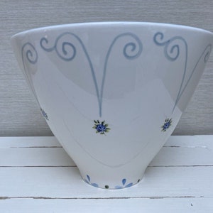 May include: A white ceramic bowl with a blue and green floral design. The bowl has a wide rim and a narrow base.