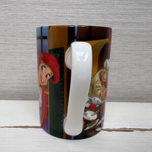 May include: A ceramic mug featuring colorful illustrations of characters from a popular animated film. The mug has a white handle and a glossy finish. The design includes a red-haired character and a chef with a white hat.