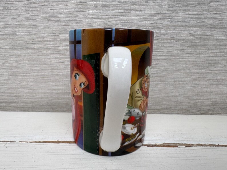 May include: A ceramic mug featuring colorful illustrations of characters from a popular animated film. The mug has a white handle and a glossy finish. The design includes a red-haired character and a chef with a white hat.