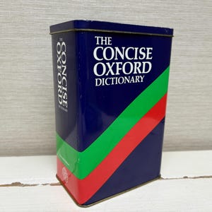 Peut inclure: Boîte métallique bleue avec l'inscription blanche "THE CONCISE OXFORD DICTIONARY". Des rayures diagonales vertes et rouges ornent la boîte, avec "CONCISE OXFORD DICTIONARY" écrit verticalement sur le côté.