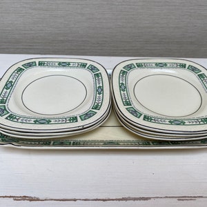 May include: A set of four vintage cream-coloured ceramic plates with a green and grey floral design. The plates are stacked on top of each other.