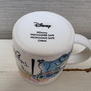 May include: White ceramic mug featuring a colorful illustration of Stitch from Disney's Lilo & Stitch. The mug has a curved handle and the text "Take Care" is visible. The bottom of the mug has the Disney logo and safety information.