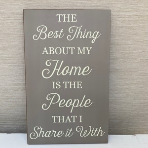 Könnte beinhalten: Ein graues Holzschild mit weißem Text, der lautet: "Das Beste an meinem Zuhause sind die Menschen, mit denen ich es teile."