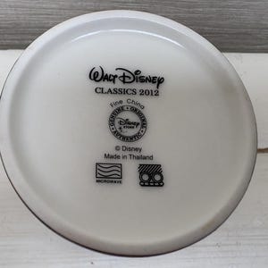 May include: A white ceramic mug base with black text that reads "Walt Disney CLASSICS 2012 Fine China Genuine Original Disney Store Authentic &copy; Disney Made in Thailand Microwave".