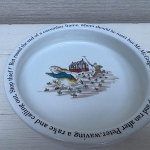 以下が含まれることがあります： ピーターラビットのイラストが描かれた白いセラミック製の子供用ボウル。ボウルには、ピーターラビットがマクレガー氏から逃げている様子が描かれており、縁には「ピーターラビットは、熊手を持って叫びながら走っている。'泥棒だ！' しかし、キュウリの枠の端を曲がると、なんとマクレガー氏に遭遇したのだ！彼は飛び上がって、ピーターラビットを追いかけて走っていった。」という文章が書かれている。