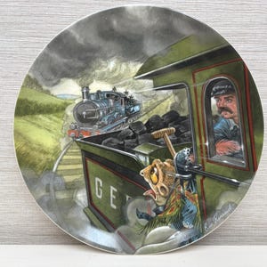 May include: Decorative plate featuring a whimsical train scene. A steam train races along tracks, with a conductor in the engine and a cartoonish creature on the side. The plate has a green and gray color scheme.