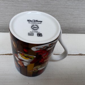 May include: White ceramic mug featuring a colorful illustration of characters from a Disney movie. The mug has a curved handle and the text "Walt Disney Classics 2012" is printed on the bottom.