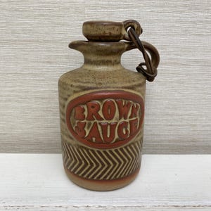 Könnte beinhalten: Eine braune Keramikflasche mit einem braunen Ledergriff und einem roten und braunen Etikett mit der Aufschrift "Brown Sauce".