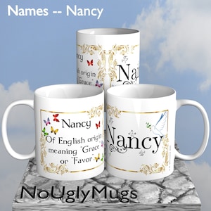 May include: Three white ceramic mugs with gold trim and a decorative design featuring butterflies and the name "Nancy". The mugs have the text "Of English origin meaning "Grace" or "Favor" printed on them. The mugs are on a textured surface with a blue sky background.