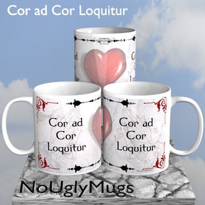 May include: Three white ceramic mugs with a black and red design. The mugs feature the text "Cor ad Cor Loquitur" and a stylized image of two hands clasped in prayer.