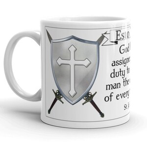 May include: White ceramic mug with a silver shield and two swords crossed behind it. The shield has a white cross on it. The text on the mug reads "Esto es lo que Dios ha asignado como deber al hombre, el bien de todos." St. Thomas Aquinas.