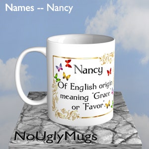 May include: White ceramic coffee mug with a gold border and butterflies. The mug has the name "Nancy" printed on it with the text "Of English origin meaning "Grace" or "Favor."