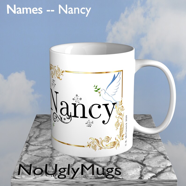 May include: White ceramic coffee mug with a gold trim and a dove with an olive branch design. The name "Nancy" is written in black script font on the mug.