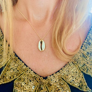 May include: A gold chain necklace with a white cowrie shell pendant.