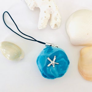 May include: A blue and white resin charm with a silver starfish, attached to a black string phone charm.