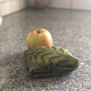 May include: A yellow and red apple rests on top of a folded green cloth with a leaf pattern. The apple is round and has a smooth surface. The cloth is folded into a square shape.