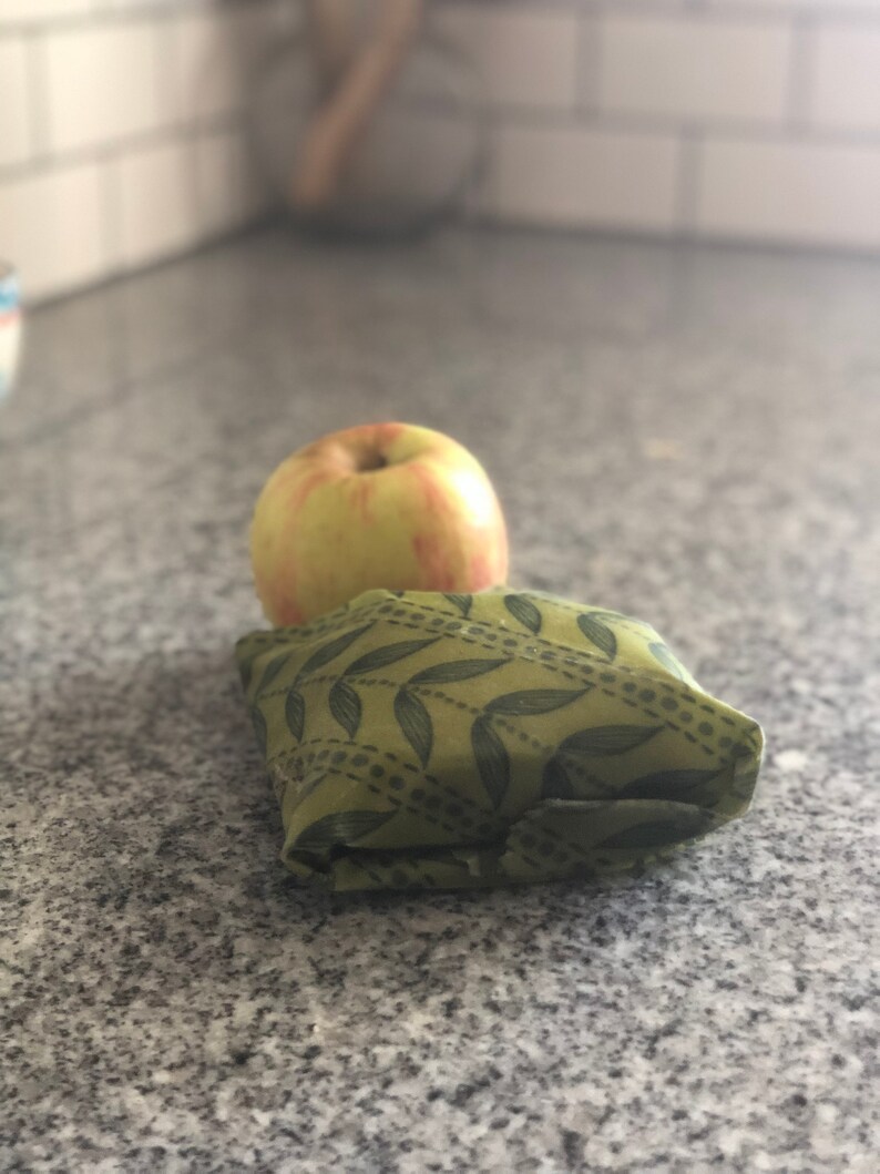 May include: A yellow and red apple rests on top of a folded green cloth with a leaf pattern. The apple is round and has a smooth surface. The cloth is folded into a square shape.